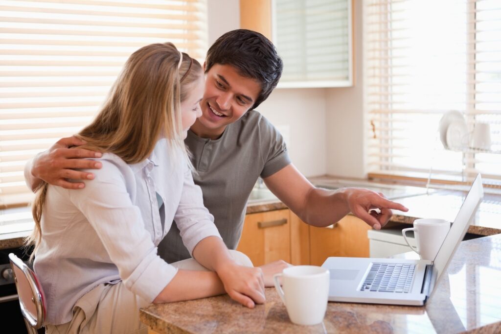Young couple reviewing online home listings together on a laptop while planning to buy their first home.