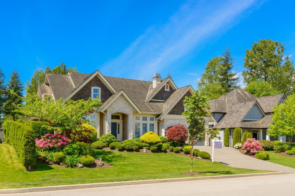 Luxury Craftsman Home with Professional Landscaping and Stone Exterior Luxury craftsman style home with stone accents, manicured landscaping, colorful flower beds, and exceptional curb appeal under a clear blue sky.